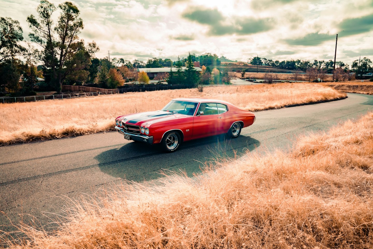 A red muscle car with black stripes parked on a road.