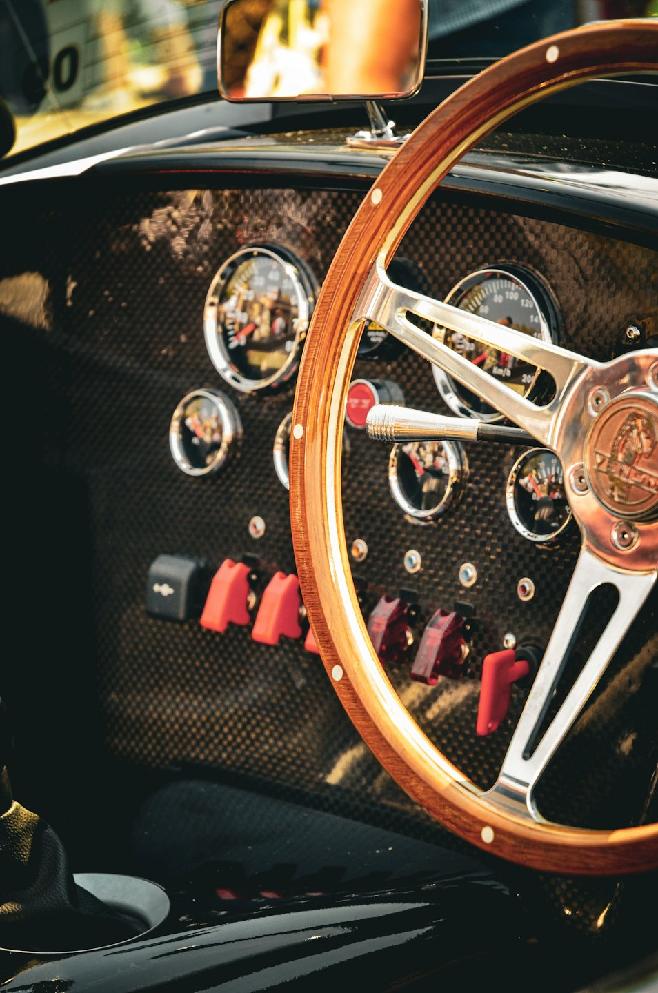 Wooden steering wheel and analog gauges in a vintage sports car.