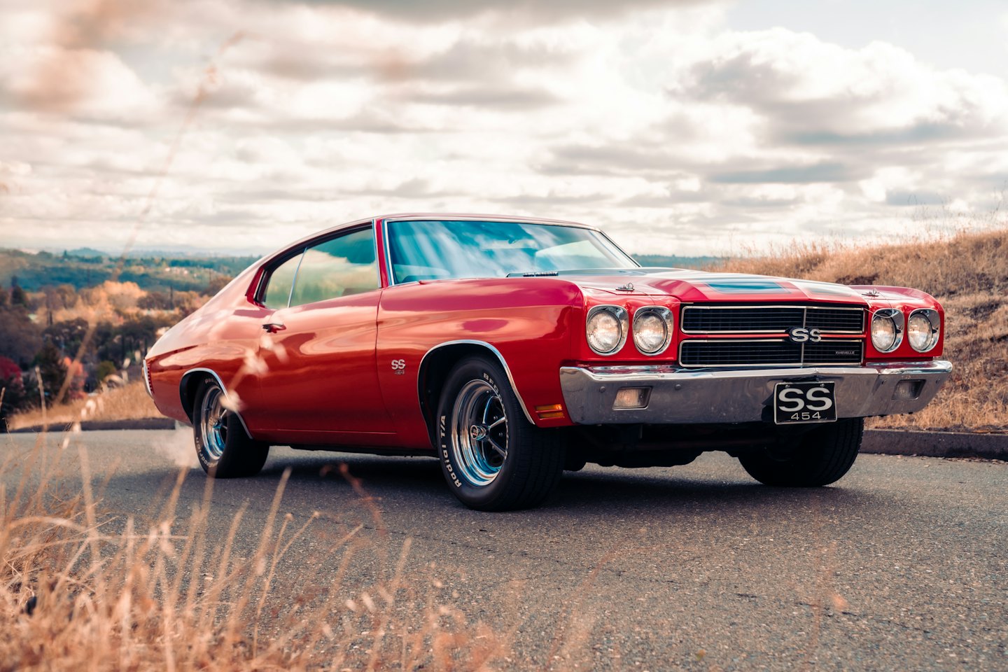 A red classic muscle car with black stripes parked on a road.