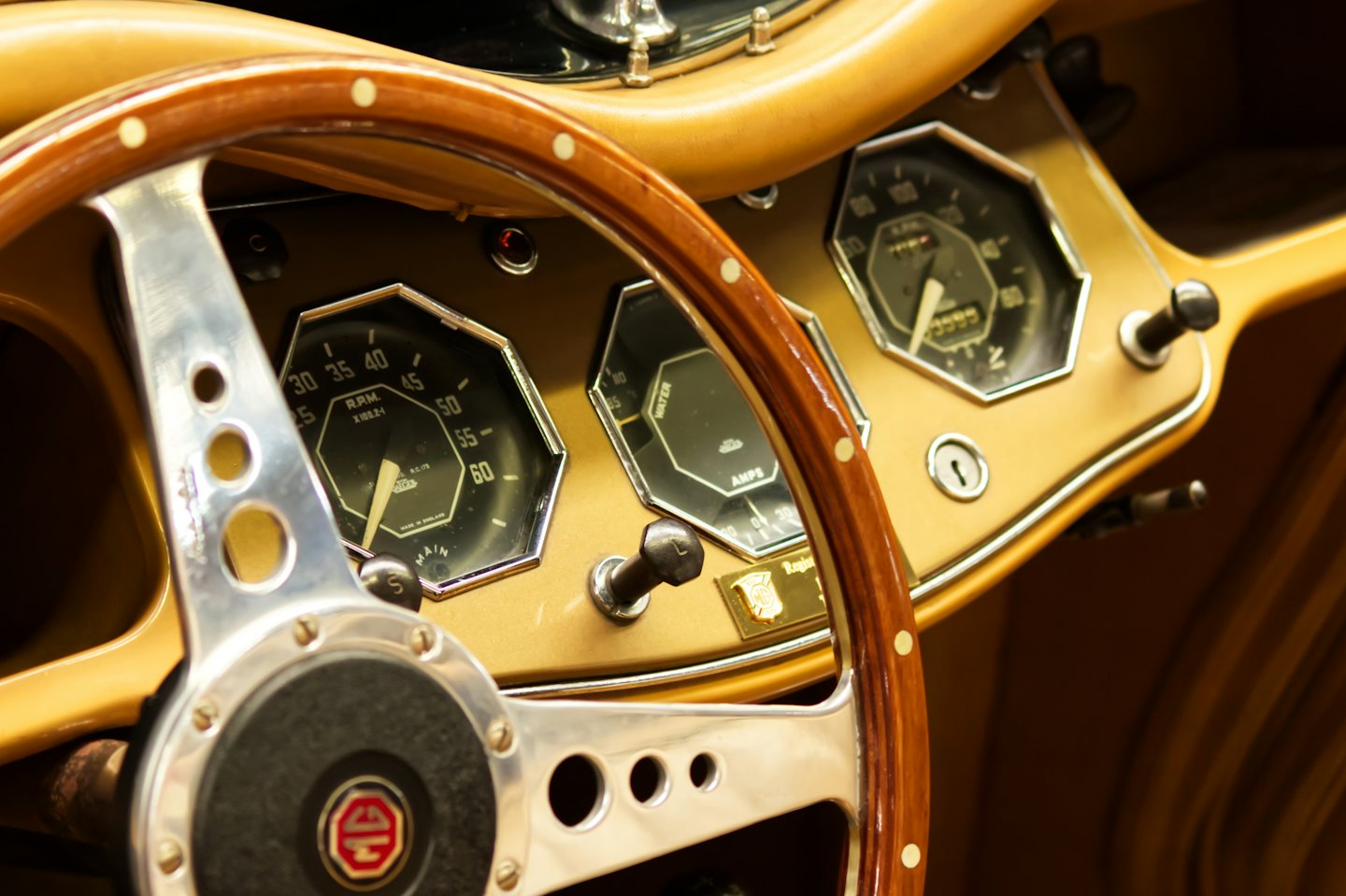Classic car dashboard with analog gauges and wooden steering wheel.