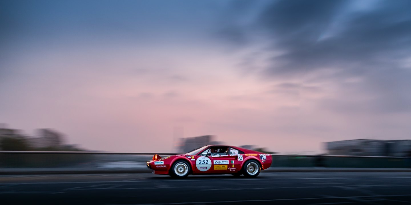 Red vintage sports car driving fast on elevated road at twilight.