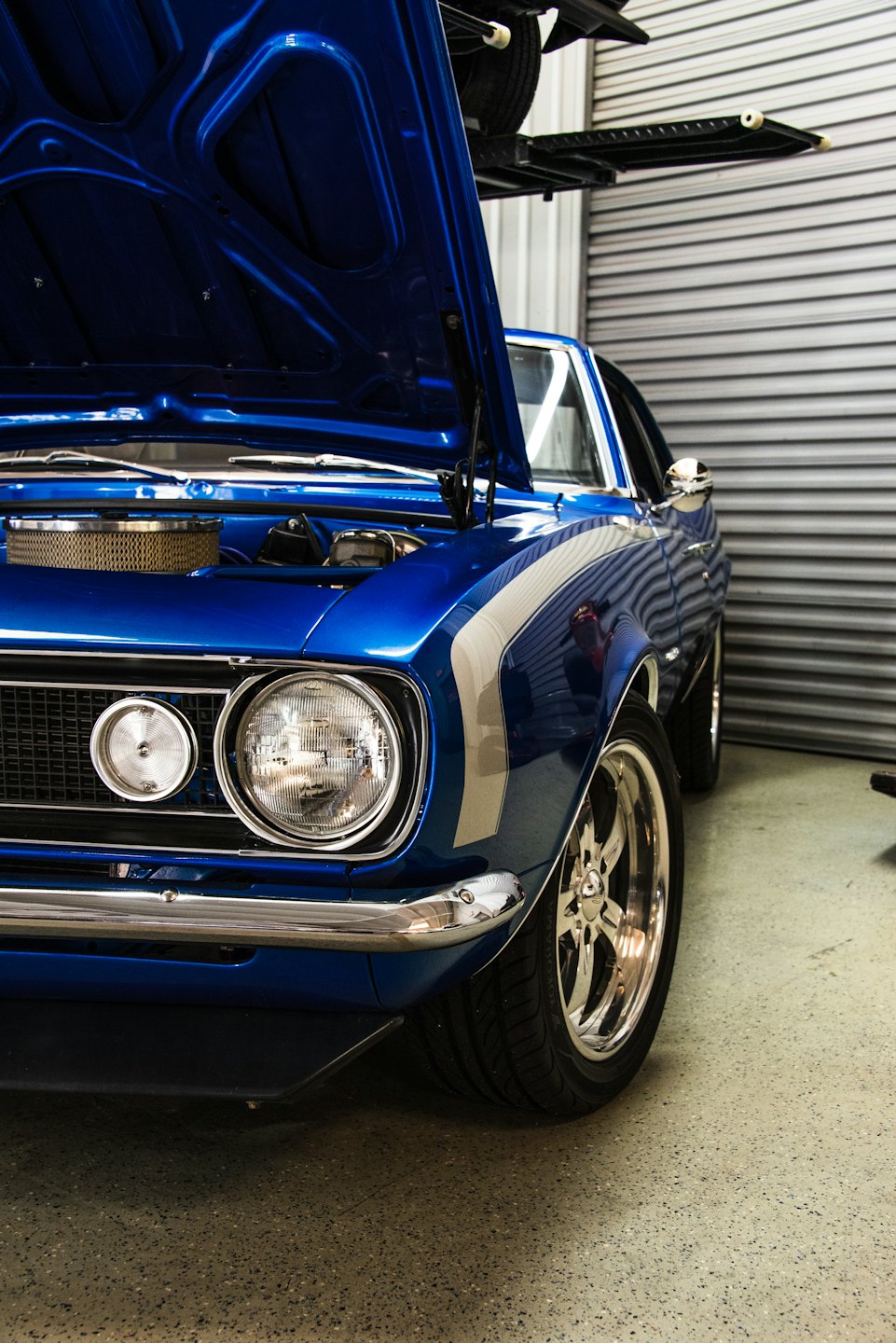 Blue vintage muscle car with open hood in a garage.