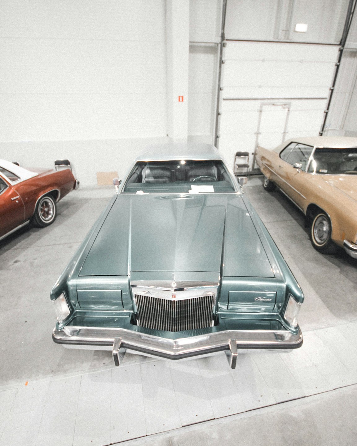 Teal classic American sedan parked inside a vehicle showroom.