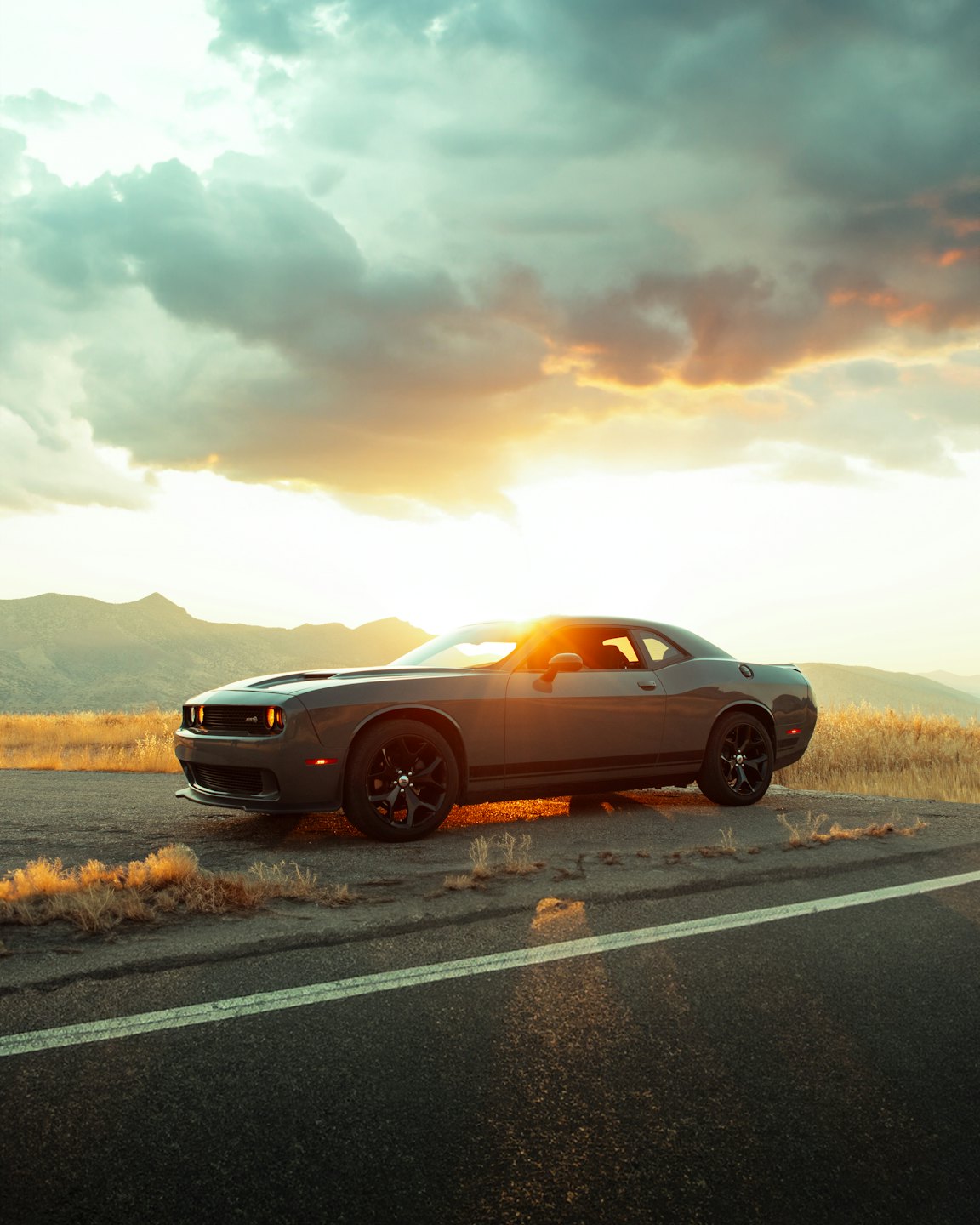 Gray muscle car parked on a roadside near mountains at sunset.